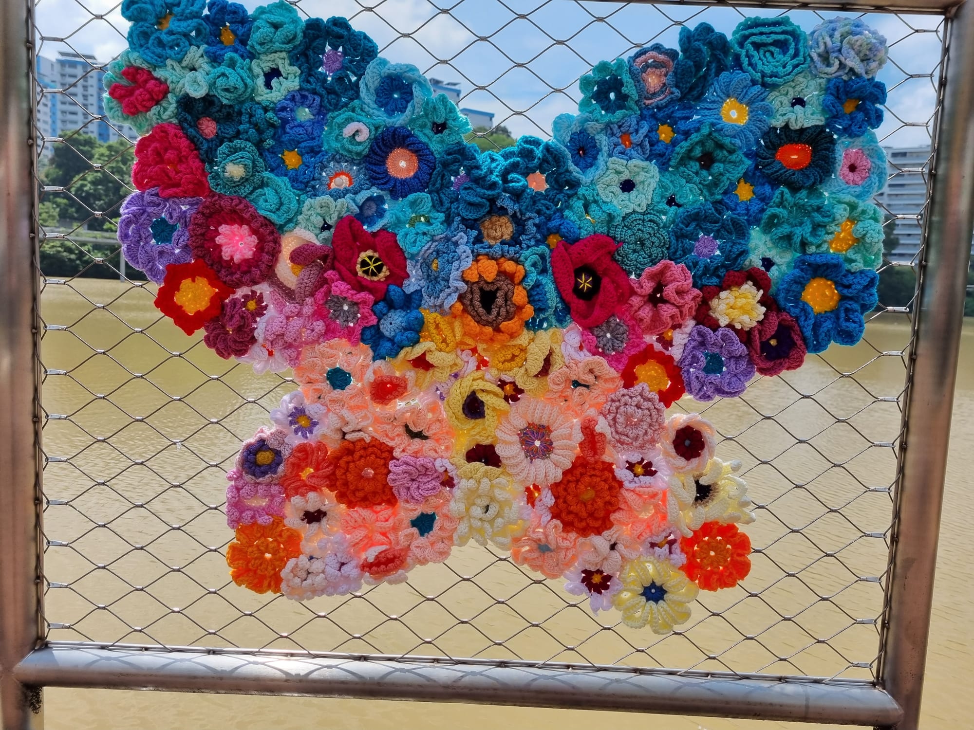 A crocheted butterfly of blue and coral flowers on the pond boardwalk railing.