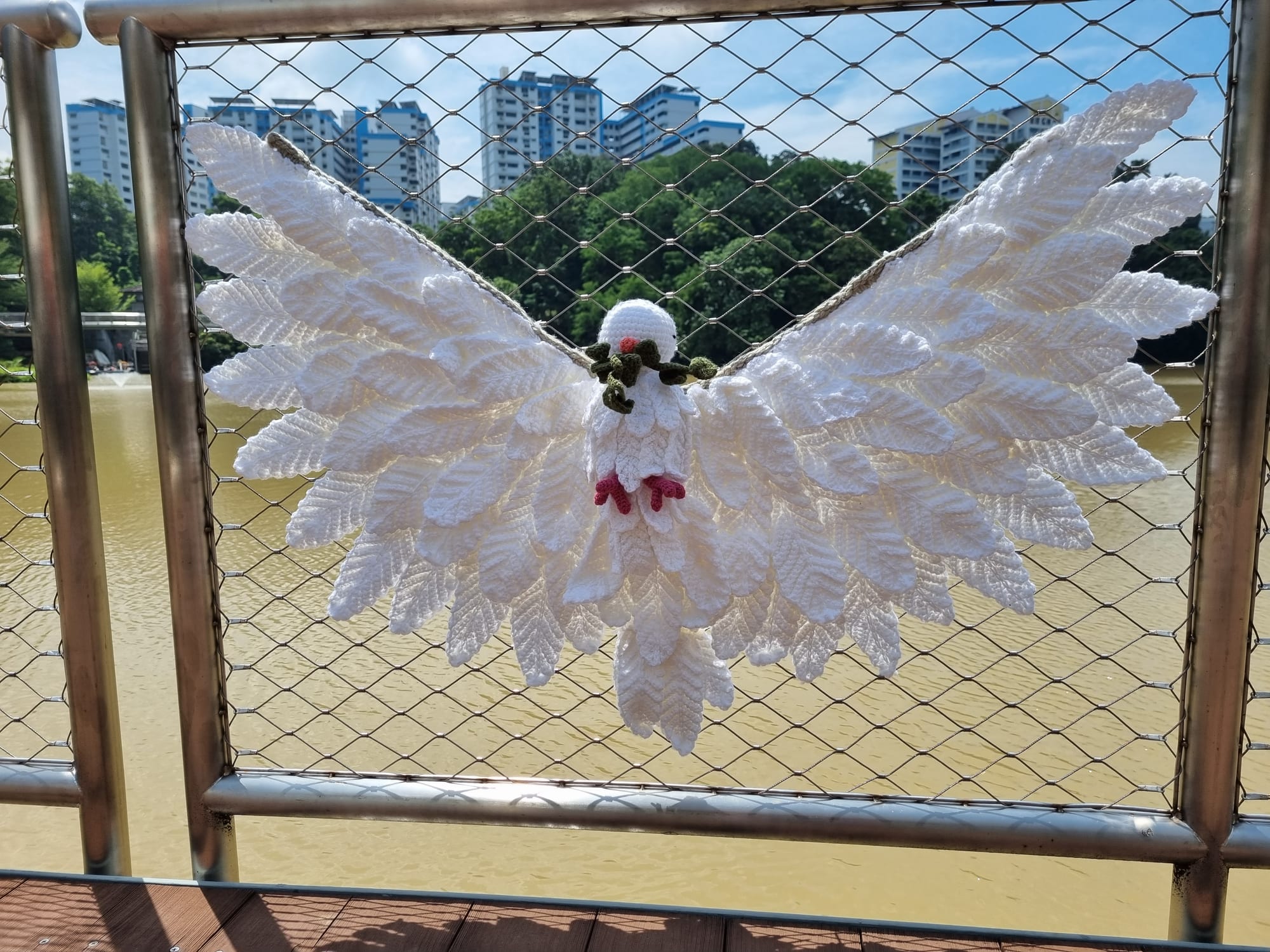 A white crocheted peace dove with outstretched wings on the pond railing.