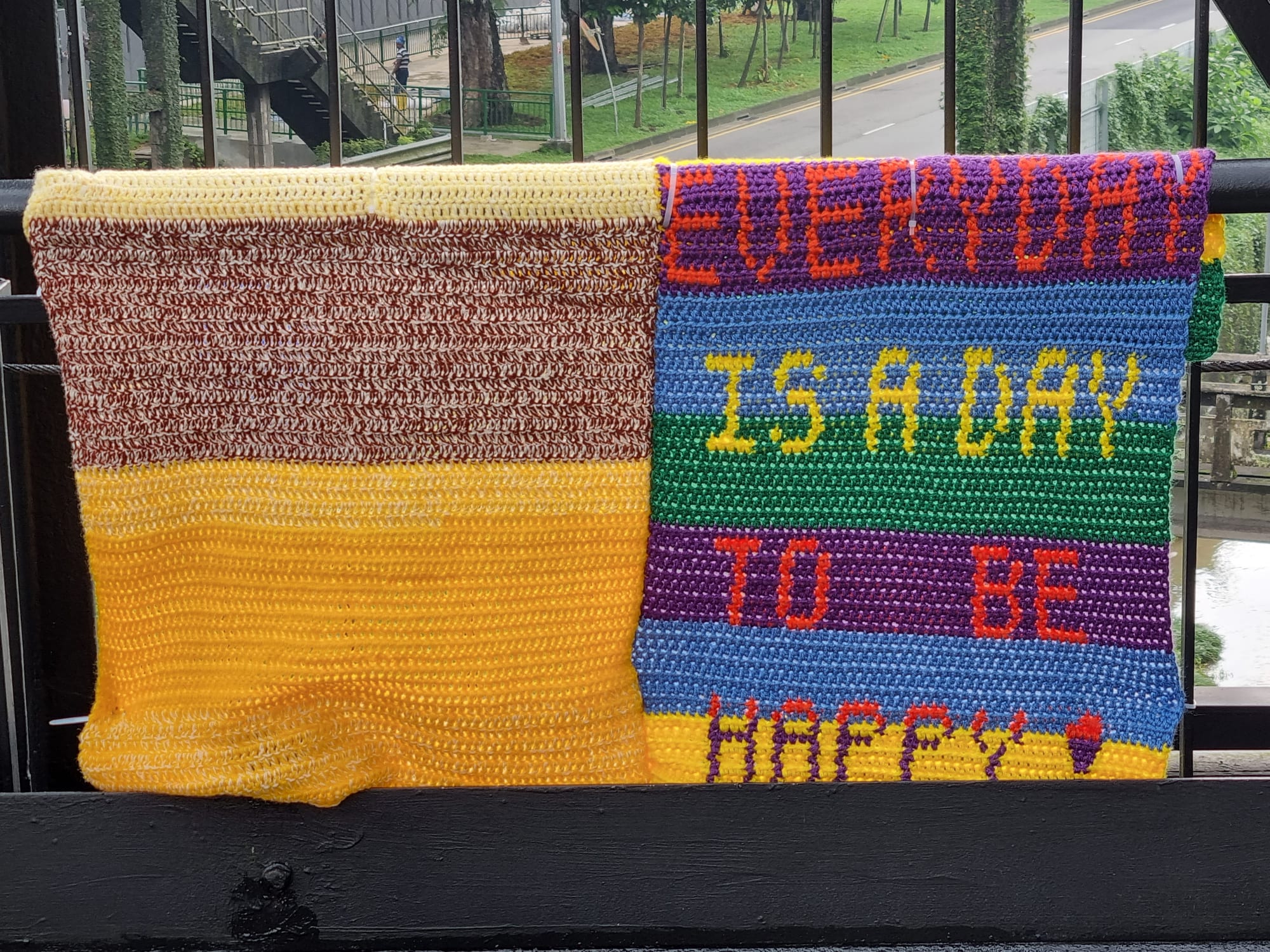 Crocheted blanket lettered "everyday is a day to be happy" on the bridge railing.