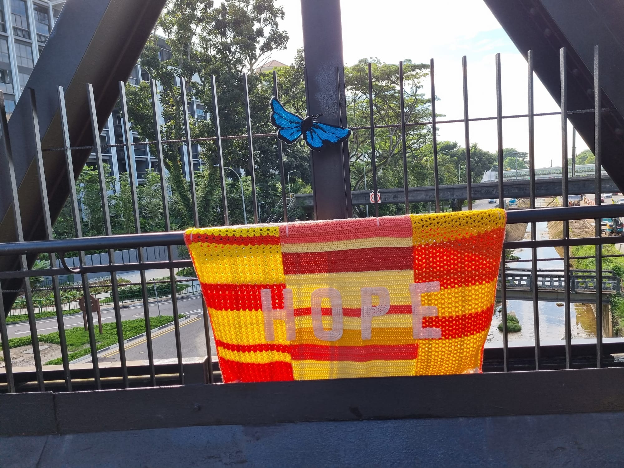 Red and yellow crocheted HOPE blanket with a blue butterfly on the bridge railing.