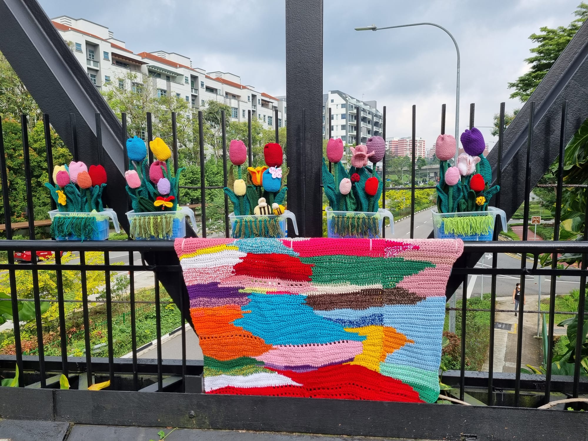 Two patchwork blankets draped along the black trusses of the bridge.