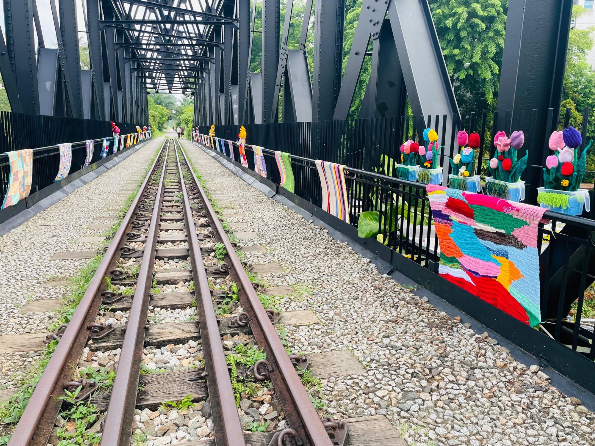 Crocheted blankets and tulips along the railings of the black steel railway truss bridge at Bukit Timah, the old track running into the distance.